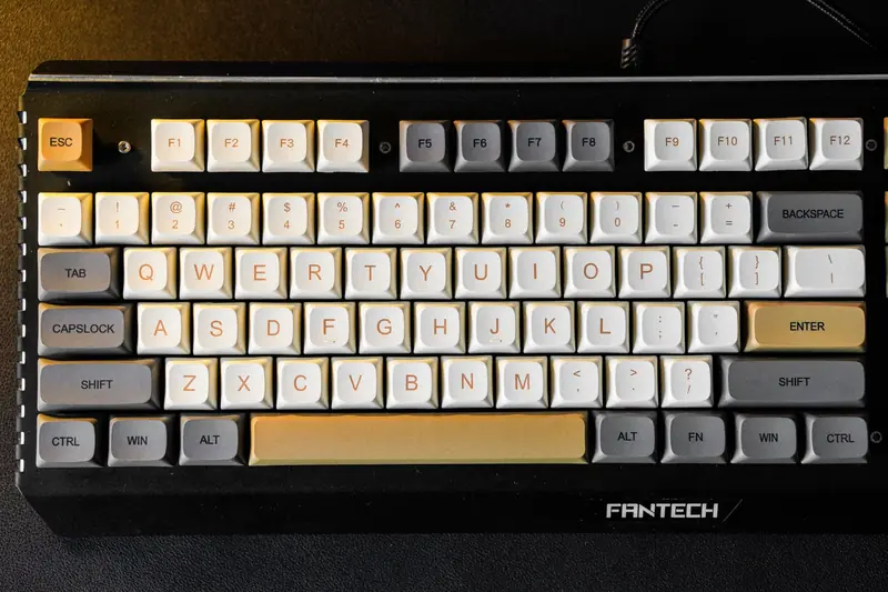 Close-up of a mechanical keyboard with custom Fantech keycaps in a color mix of beige, gray, and white