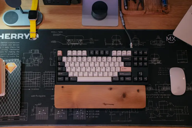 A clean and organized workspace featuring a mechanical keyboard on a custom desk mat with tech accessories