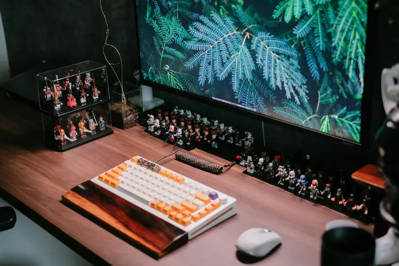 Modern desk setup featuring a custom keyboard, monitor, and collectible figurines for a tech-savvy workspace