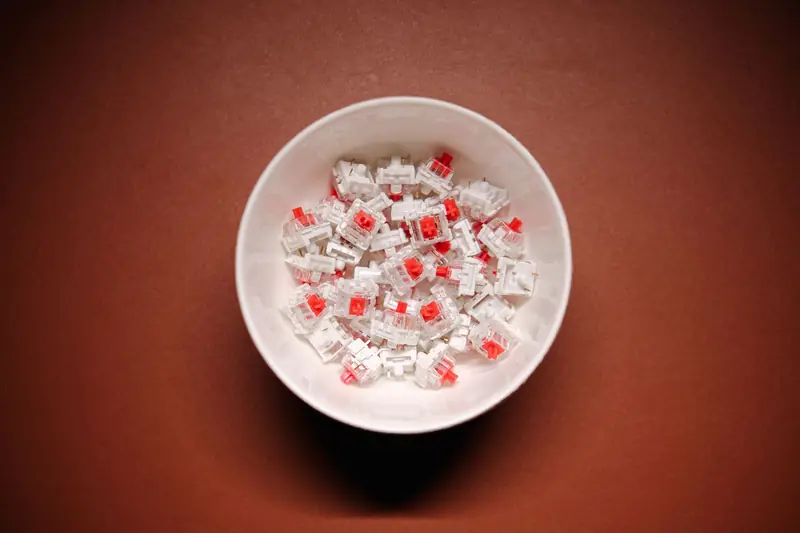 Top view of mechanical keyboard switches in a bowl on a brown surface