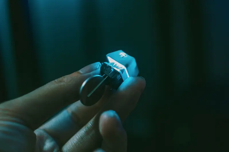 A close-up view of a hand holding a mechanical keyboard switch with a keycap attached