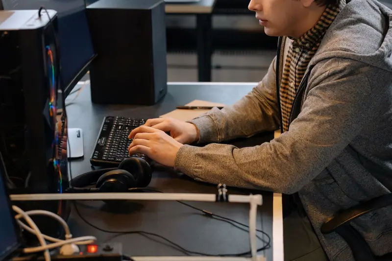 Focused young adult typing on keyboard at modern workspace with headphones nearby