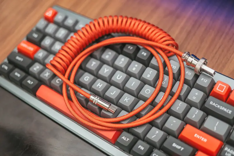 Close-up of a custom coiled cable resting on a mechanical keyboard, showcasing modern technology aesthetics