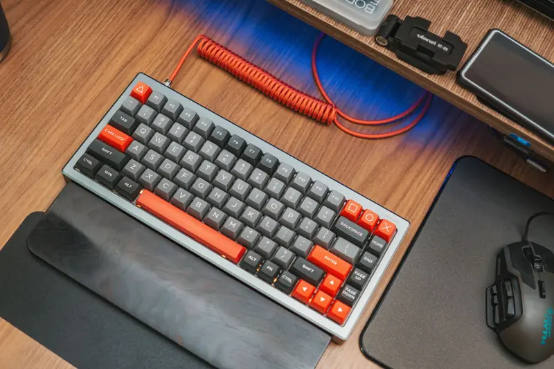 Modern mechanical keyboard with red accents on wooden desk, captured from above