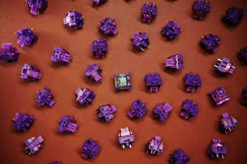 Flat lay of purple mechanical keyboard switches scattered on a brown surface