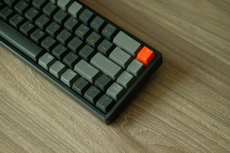 A detailed view of a mechanical keyboard with orange accent key on a wooden table