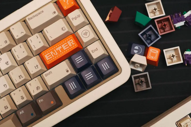 Top view of a beige mechanical keyboard with colorful custom keycaps and loose switches nearby