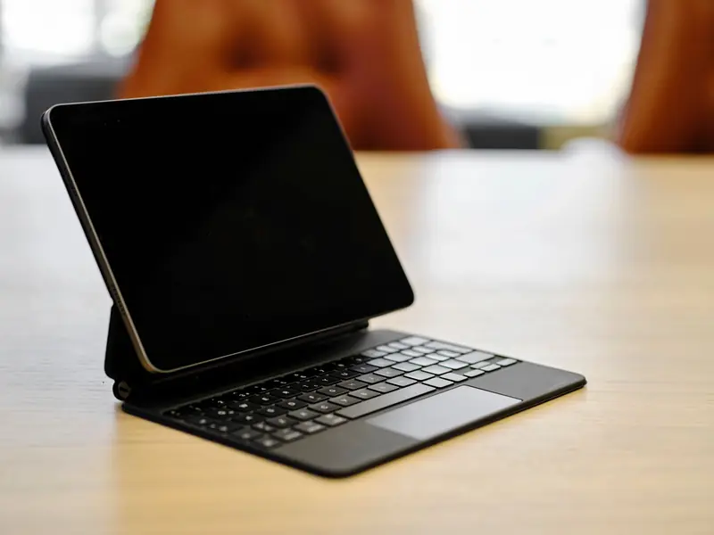 A digital tablet attached to a keyboard case on a wooden table in an office setting